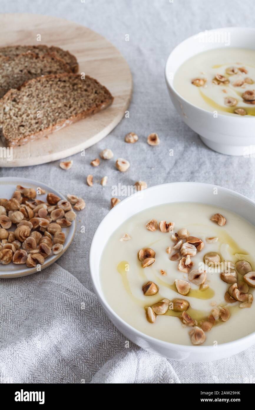Celeriac and hazelnut soup in a white ceramic bowl with a board of Irish brown bread in the background. Stock Photo