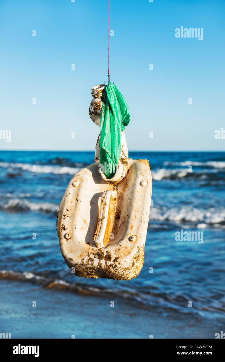 closeup of some used plastic objects in a fish hook, freshly fished in the ocean, in front of the water Stock Photo