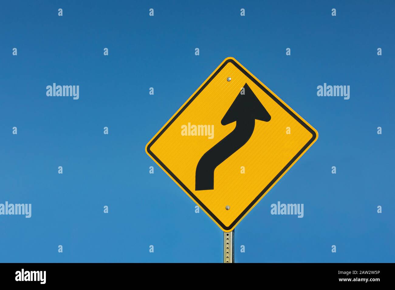 Yellow reflective winding road ahead traffic sign isolated on sunny blue sky background Stock Photo