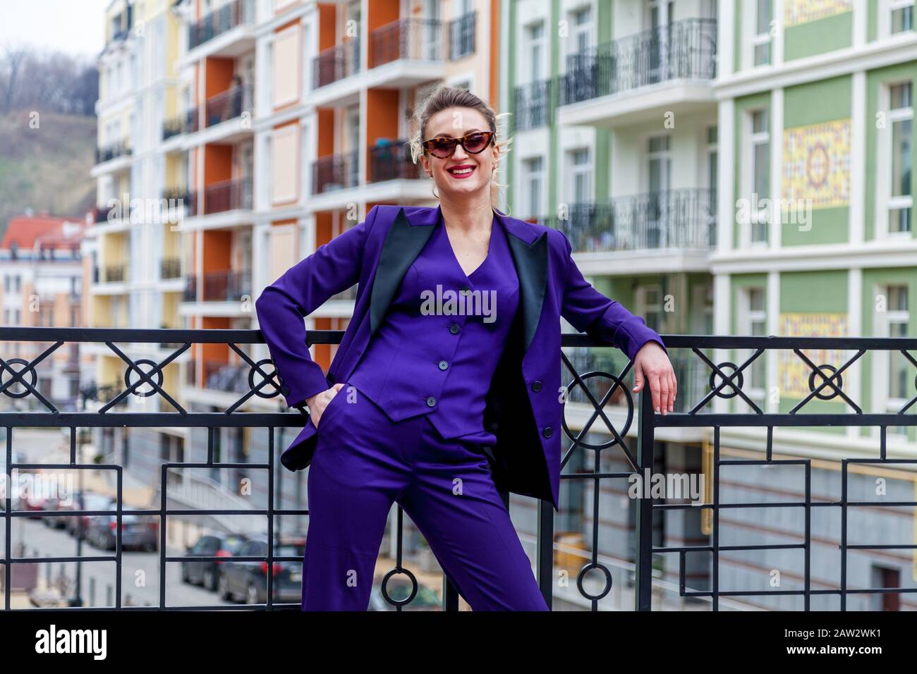 A portrait of a blond woman wearing in a purple suit and glasses poses ...