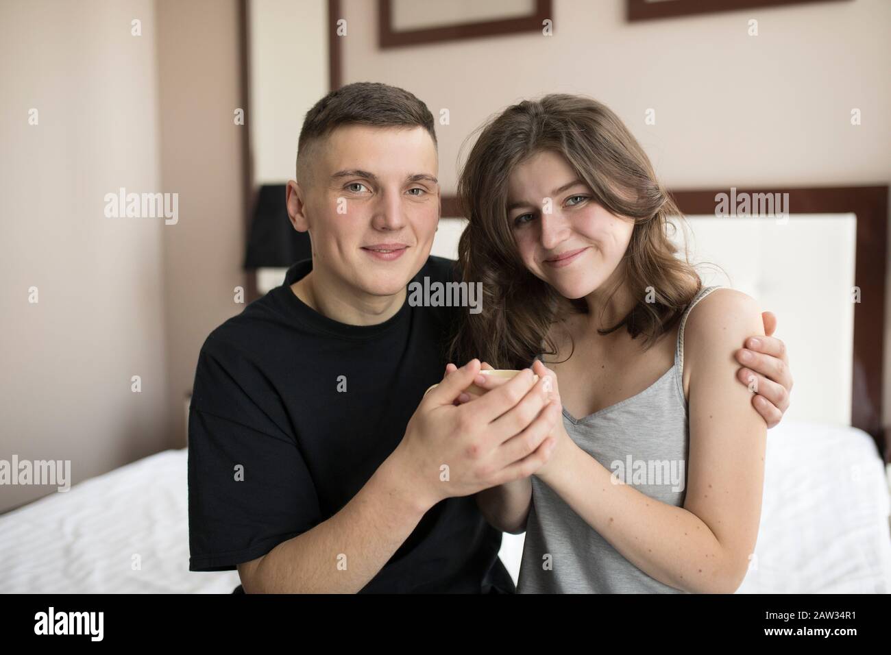 Smiling young man embracing girlfriend and looking at camera. Stock Photo