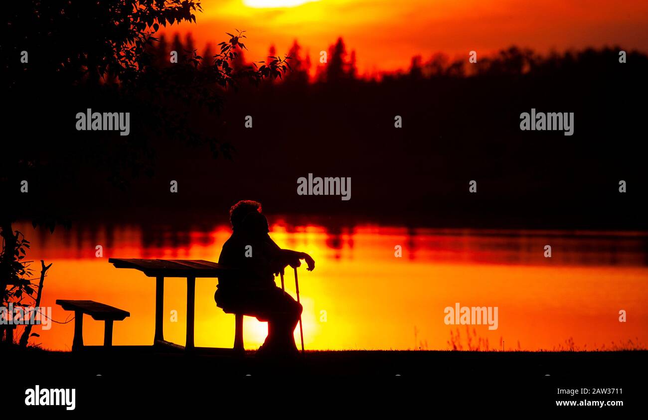 Two people sitting on bench at sunset by lake Stock Photo - Alamy