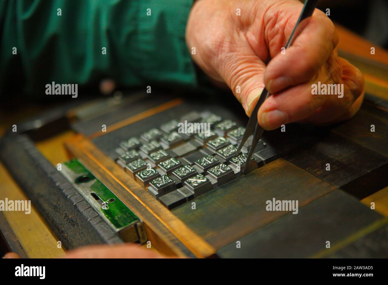 A man uses tweezers to arrange decorative metal type Stock Photo