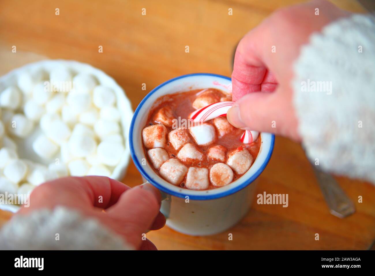 A woman holds a candy cane in a mug of hot chocolate with marshmallows Stock Photo