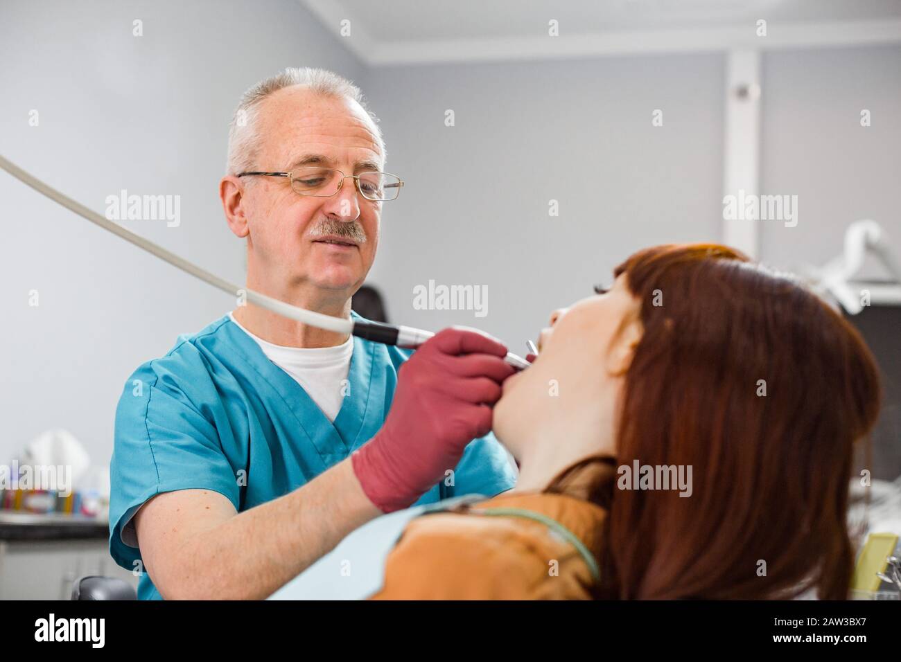 Smiling senior experienced man dentist performing dental treatment of patients tooth. Young woman at the dentist's chair during a dental procedure. Stock Photo