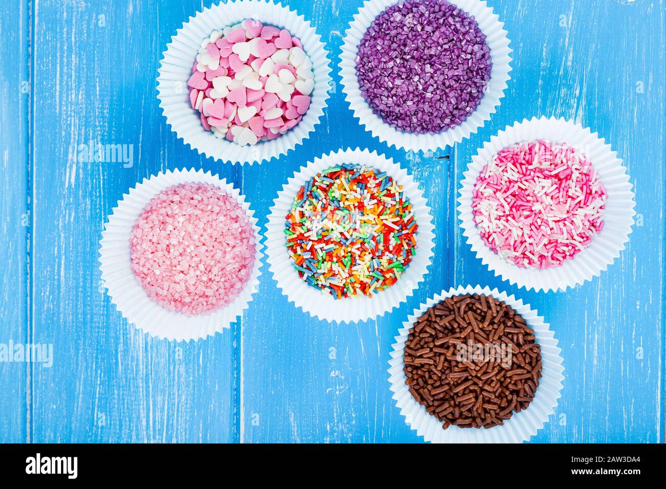 Colorful candy sprinkles on the paper cupcake holder. Blue wooden rustic background. Stock Photo