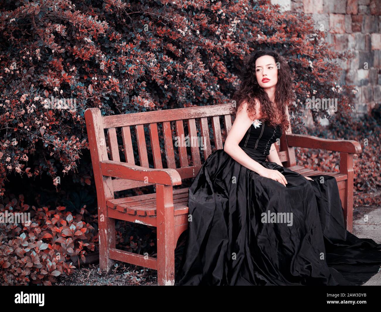 Beautiful elegant woman wearing black dress and sitting on a bench Stock Photo