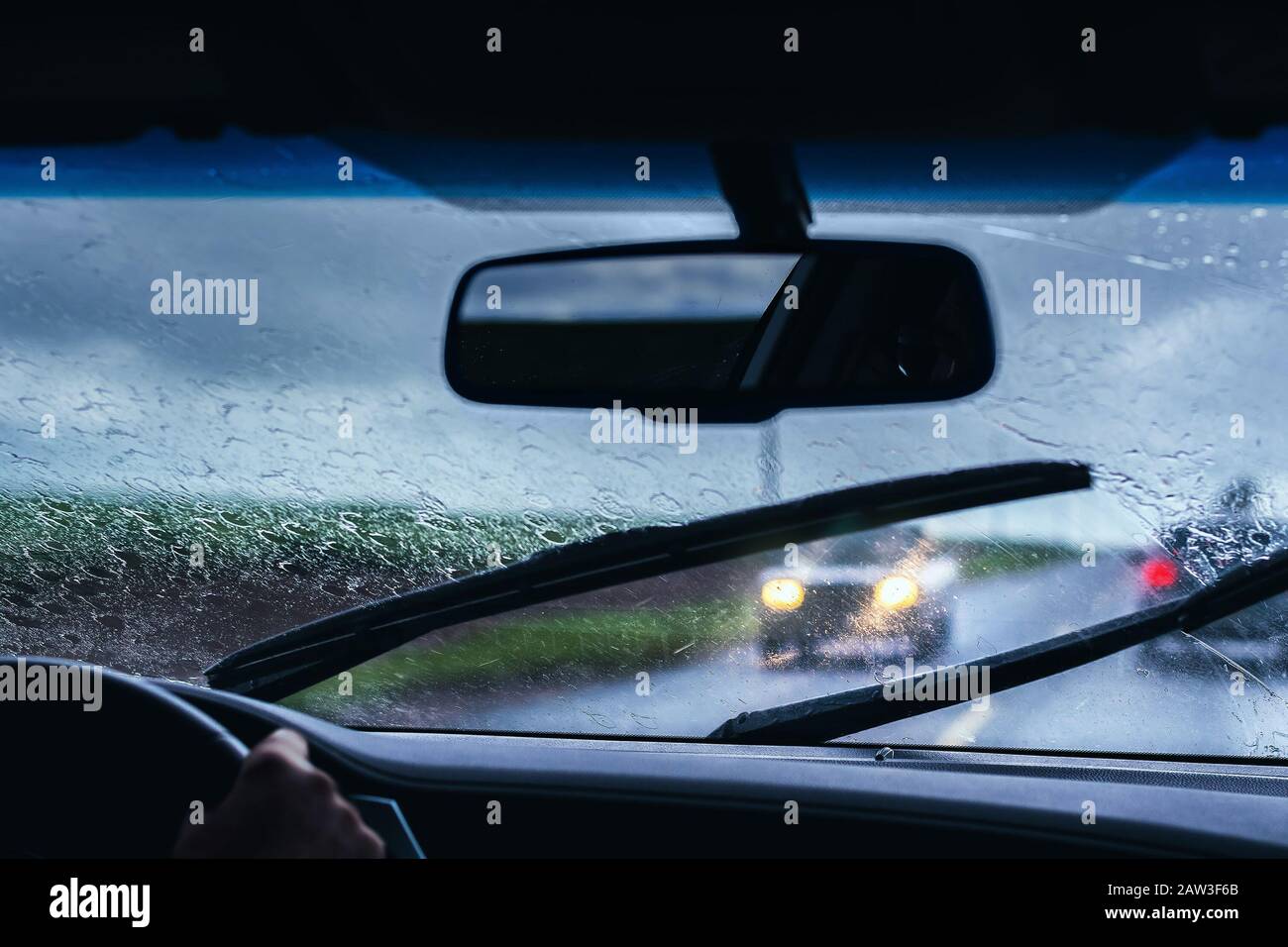 Driving carefully a car on the road on a rainy day, traffic of cars on the road. Windshield of a car wet by the rain, wiper blades cleaning the front Stock Photo