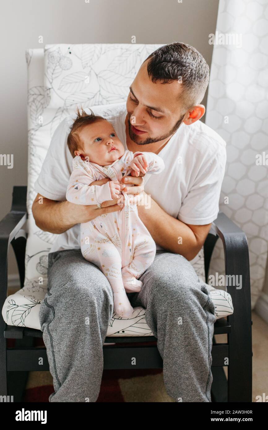 Caucasian father sitting in armchair with newborn baby girl. Parent
