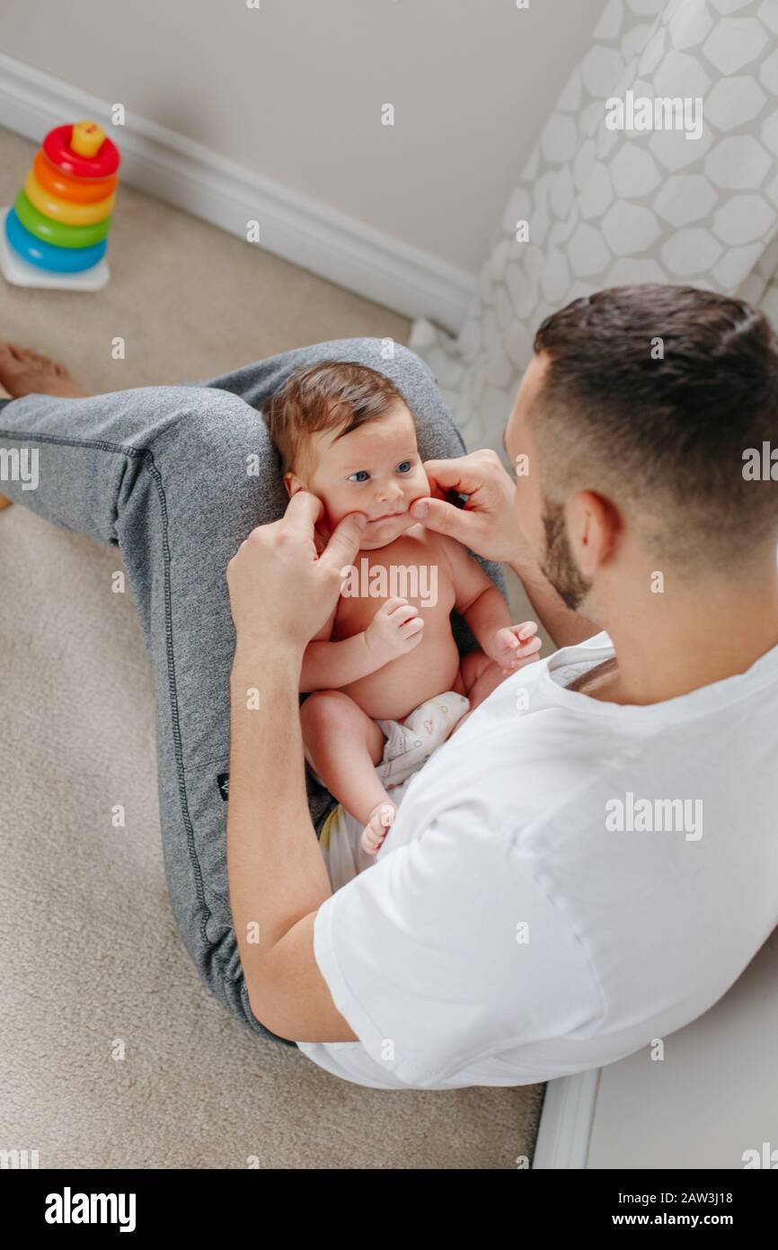 Happy Caucasian father holding newborn baby on laps knees. Man parent