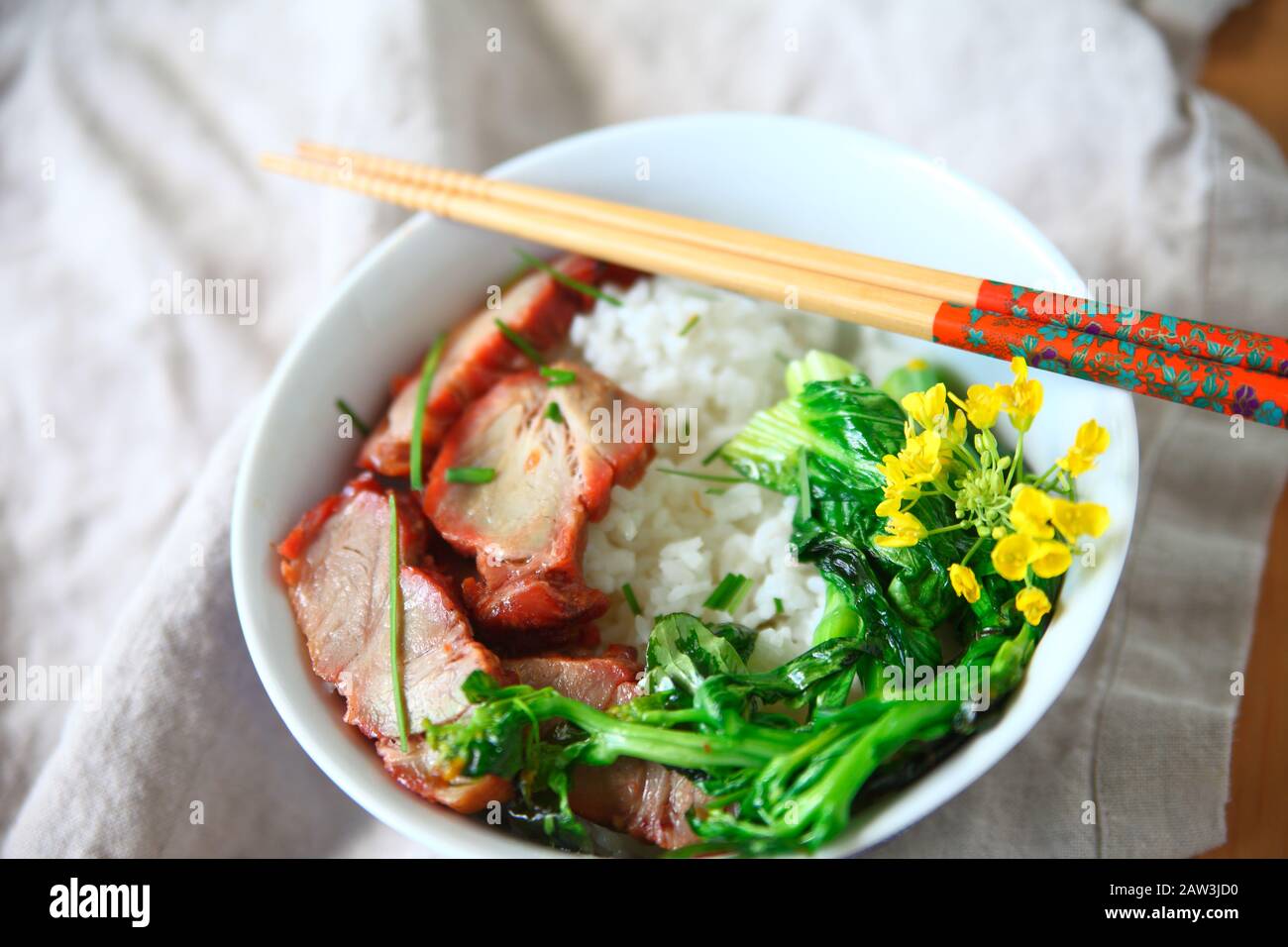 Roast pork and Asian greens with edible flowers on rice Stock Photo