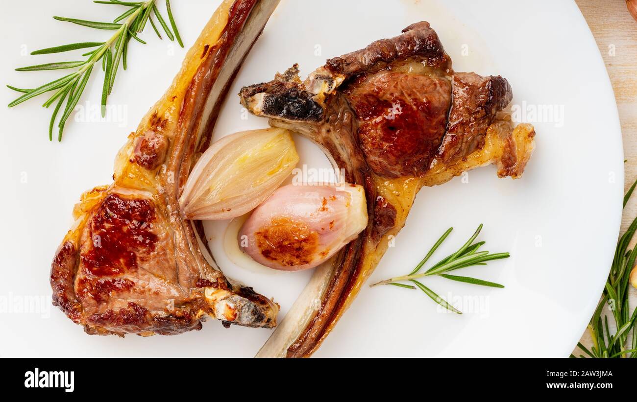 fried lamb ribs on white plate with vegetable and seasoning on white marble table, top view