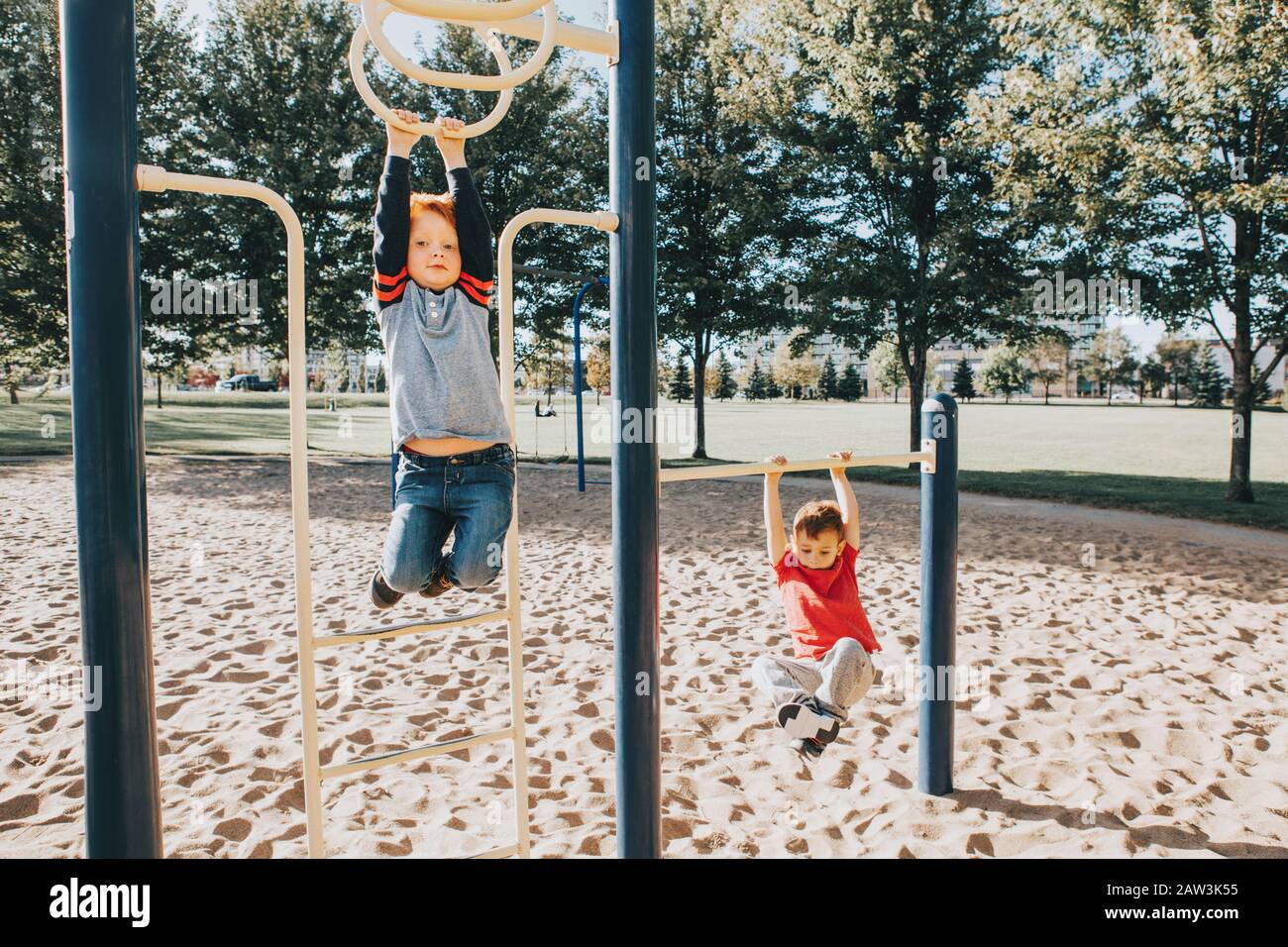 Young Caucasian boys friends hanging on monkey bars and pull-up bars in park on playground. Summer outdoor activity for kids. Active children doing ex Stock Photo