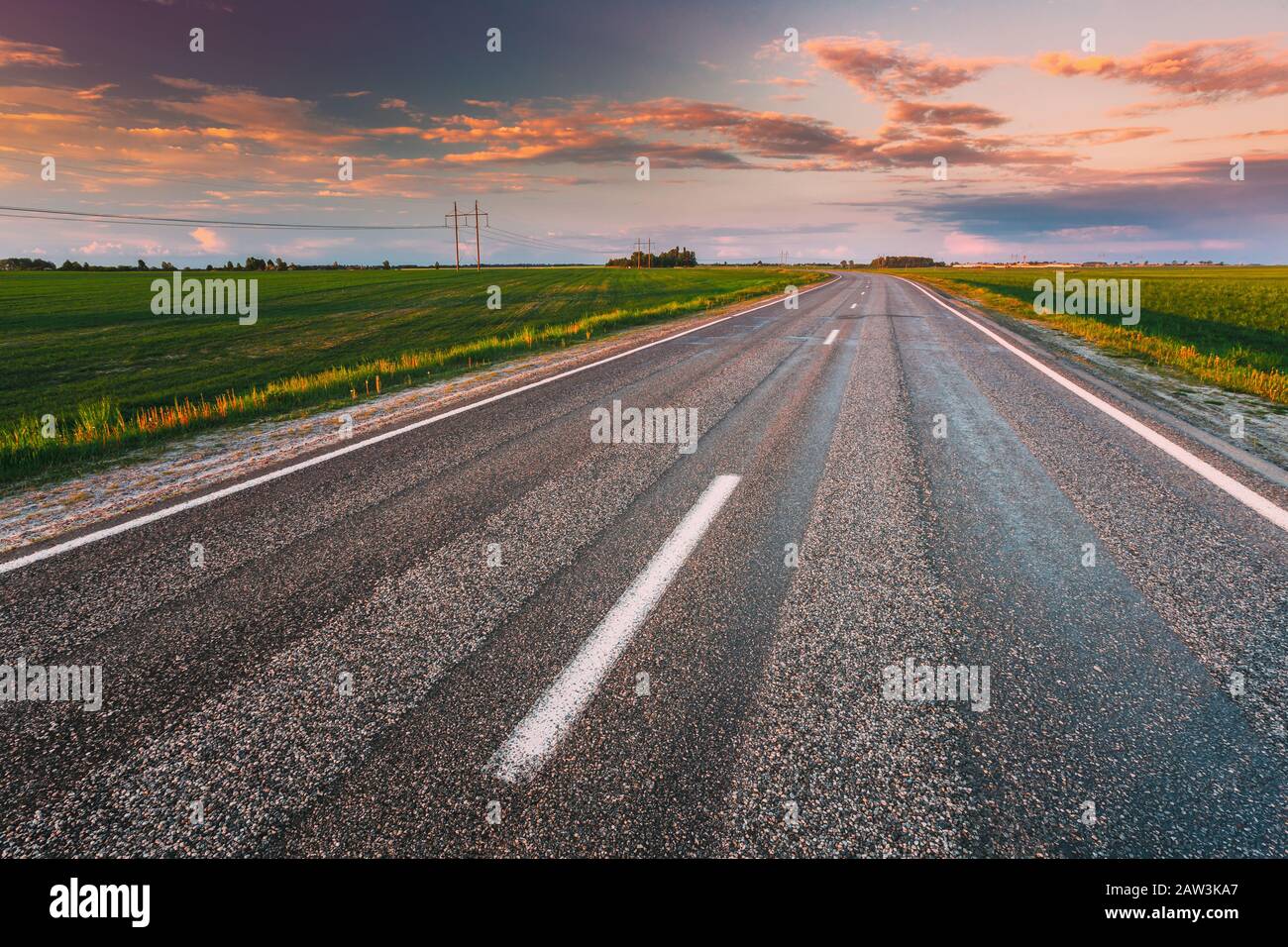 Asphalt Country Open Road Through Spring Fields And Meadows In Sunny Evening. Landscape In Early Summer Season At Sunny Sunset. Stock Photo
