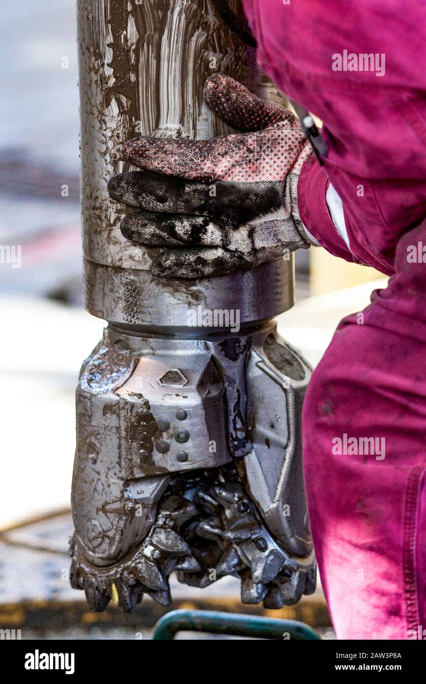 worker guides drill bit into drill hole on drill floor Stock Photo