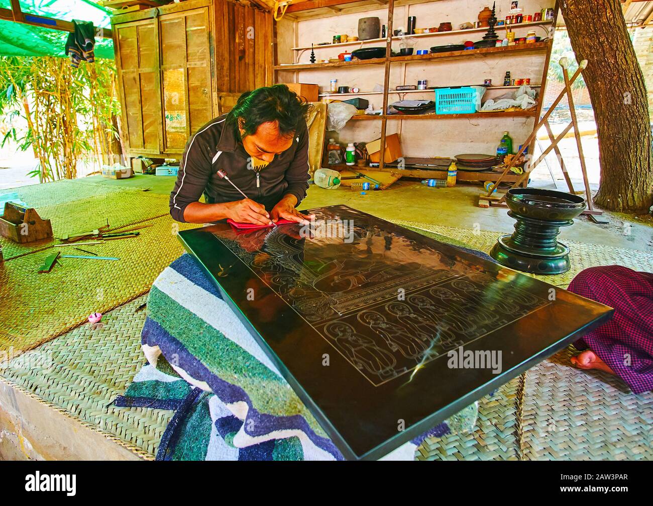 BAGAN, MYANMAR - FEBRUARY 25, 2018: The artisan of the local lacquerware workshop scratches the lacquer panel with etching needle to create a picture, Stock Photo