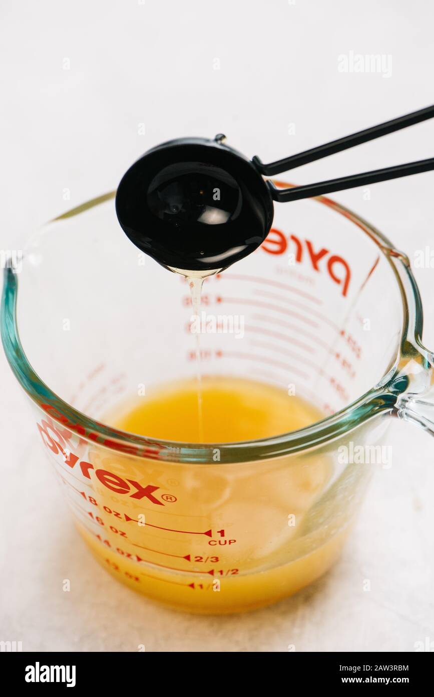 Measuring spoon is used to add oil to a pyrex measuring cup recipe Stock Photo