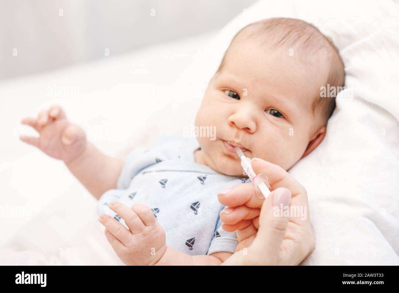 Mother feeding newborn baby with Vitamin K using plastic syringe to