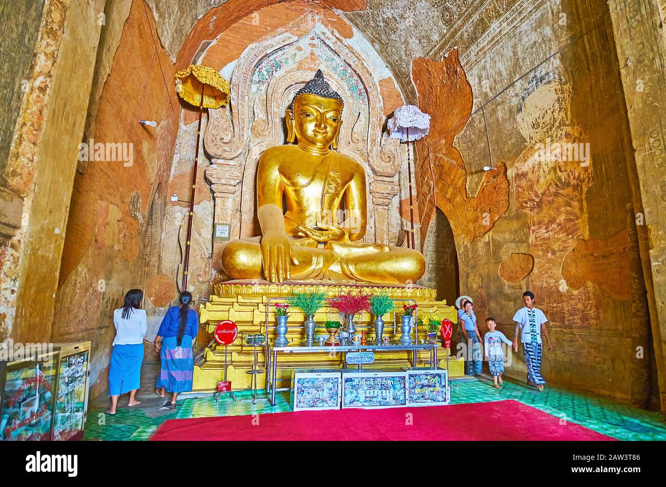 BAGAN, MYANMAR - FEBRUARY 25, 2018:  The Htilominlo Temple prayer hall with amazing golden image of Buddha, surrounded by ancient frescoes and molding Stock Photo