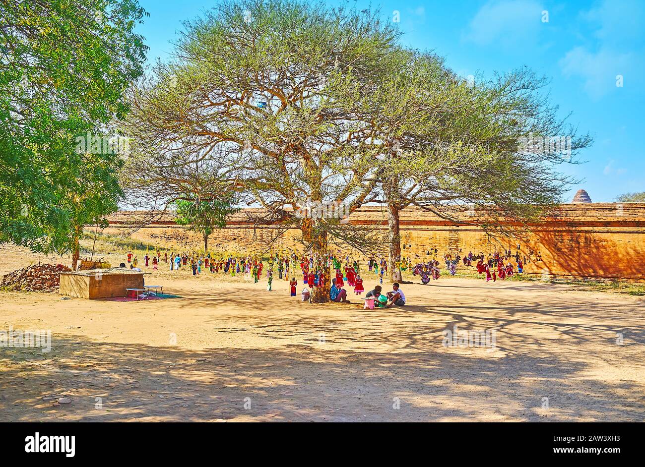 BAGAN, MYANMAR - FEBRUARY 25, 2018:  The spread shady tree with numerous hanging string puppets of market stall at the wall of Dhammayangyi Pagoda, on Stock Photo