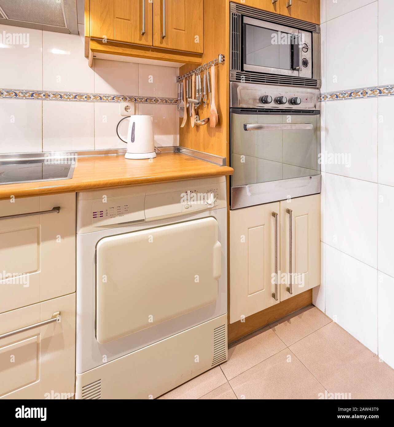 New stylish bright kitchen with wooden cabinets, microwave and oven. Spacious modern fully equipped appliance interior with wooden desk, ceramic stove Stock Photo