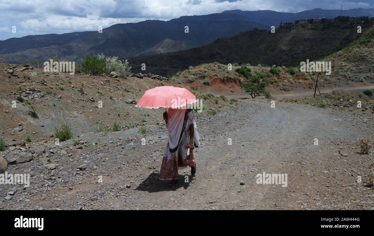 Ethiopian woman walks up a dry track protecting herself from the harsh midday sun under a pink umbrella Stock Photo