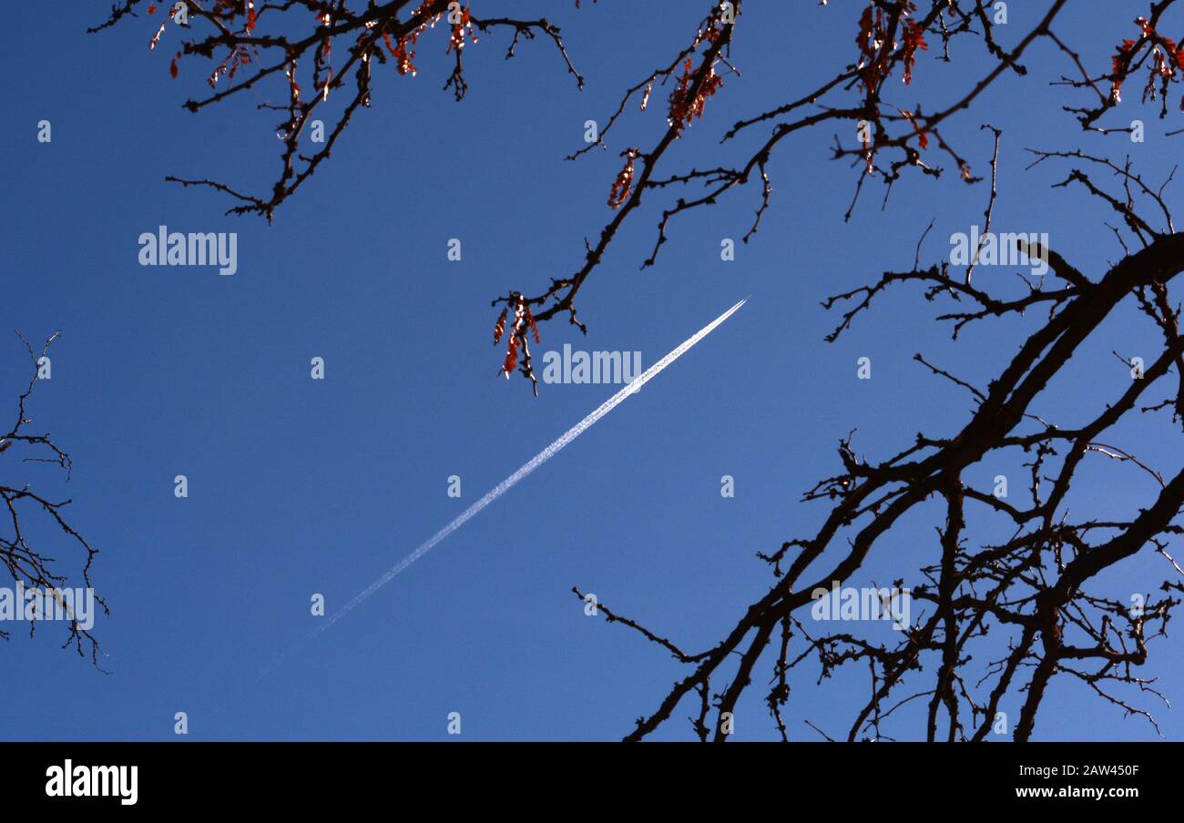 A jet aircraft leaves vapor trails, or contrails, streaking across the sky. Stock Photo