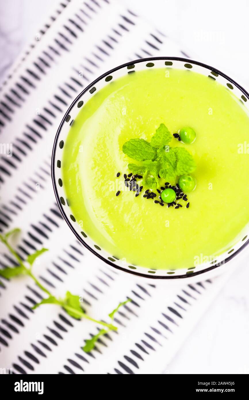 Homemade green cream soup with green peas, mint, black cumin or nigella sativa on a light background, top view Stock Photo