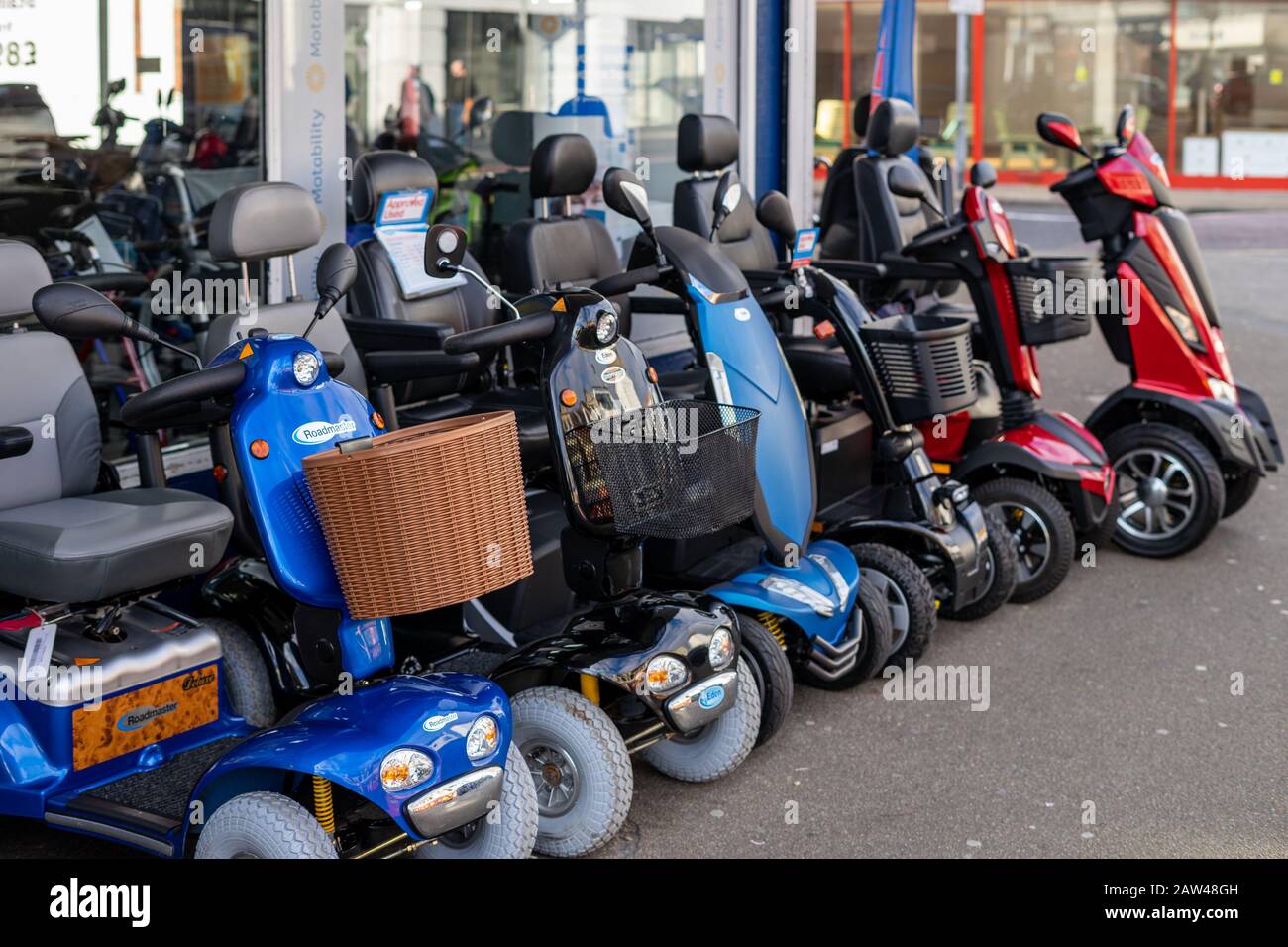 A row of mobility scooters or disability scooters outside a shop on sale Stock Photo