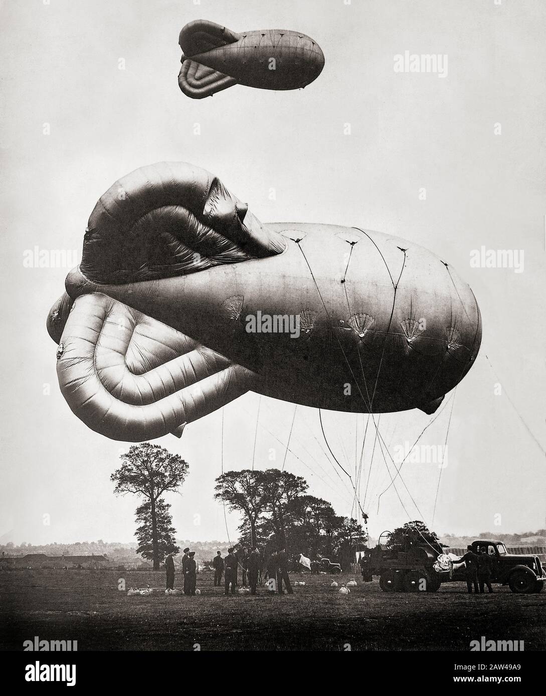 A pair of Low Zone barrage balloons. In 1938, British Balloon Command was established to protect cities and key targets such as industrial areas, ports and harbours. The large tethered kite balloons defended ground targets against aircraft attack, by raising aloft steel cables which pose a severe collision risk to aircraft, making the attacker's approach more difficult, forcing them to fly higher and into the range of concentrated anti-aircraft fire. Stock Photo