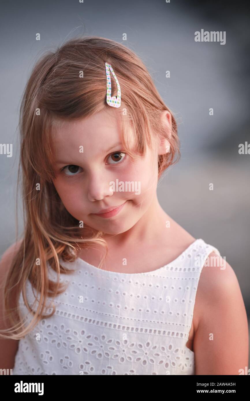 Serious blond little girl in white dress, close-up vertical outdoor portrait Stock Photo