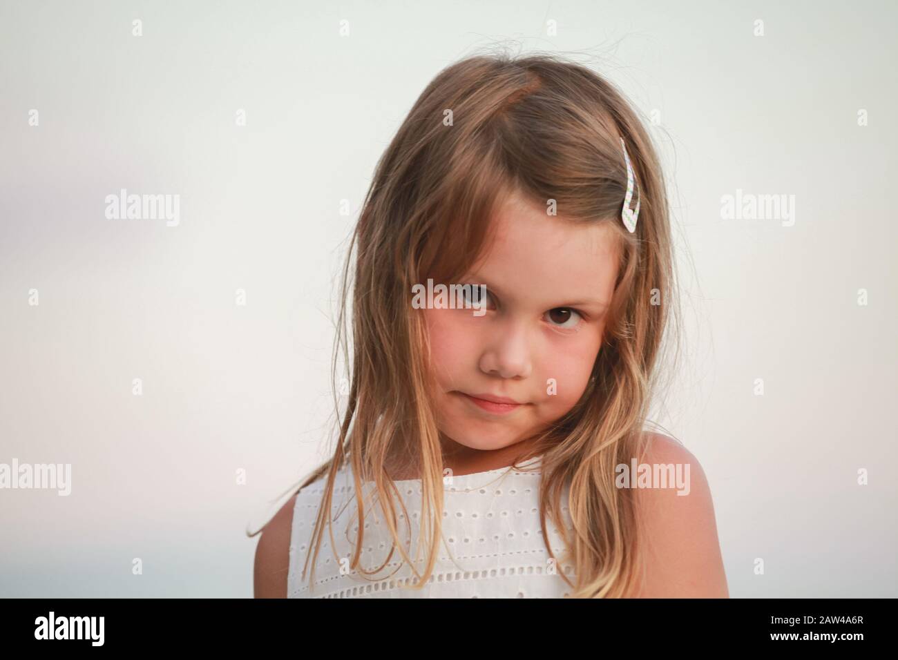 Serious blond little girl in white dress, close-up outdoor face portrait Stock Photo