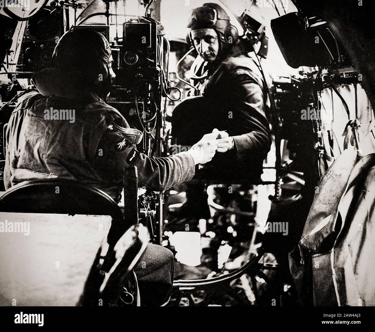 Inside the cockpit of a Wellington Mark I heavy bomber flying during the early years of the war, a wireless operator passes a recently received message to the second pilot. Stock Photo