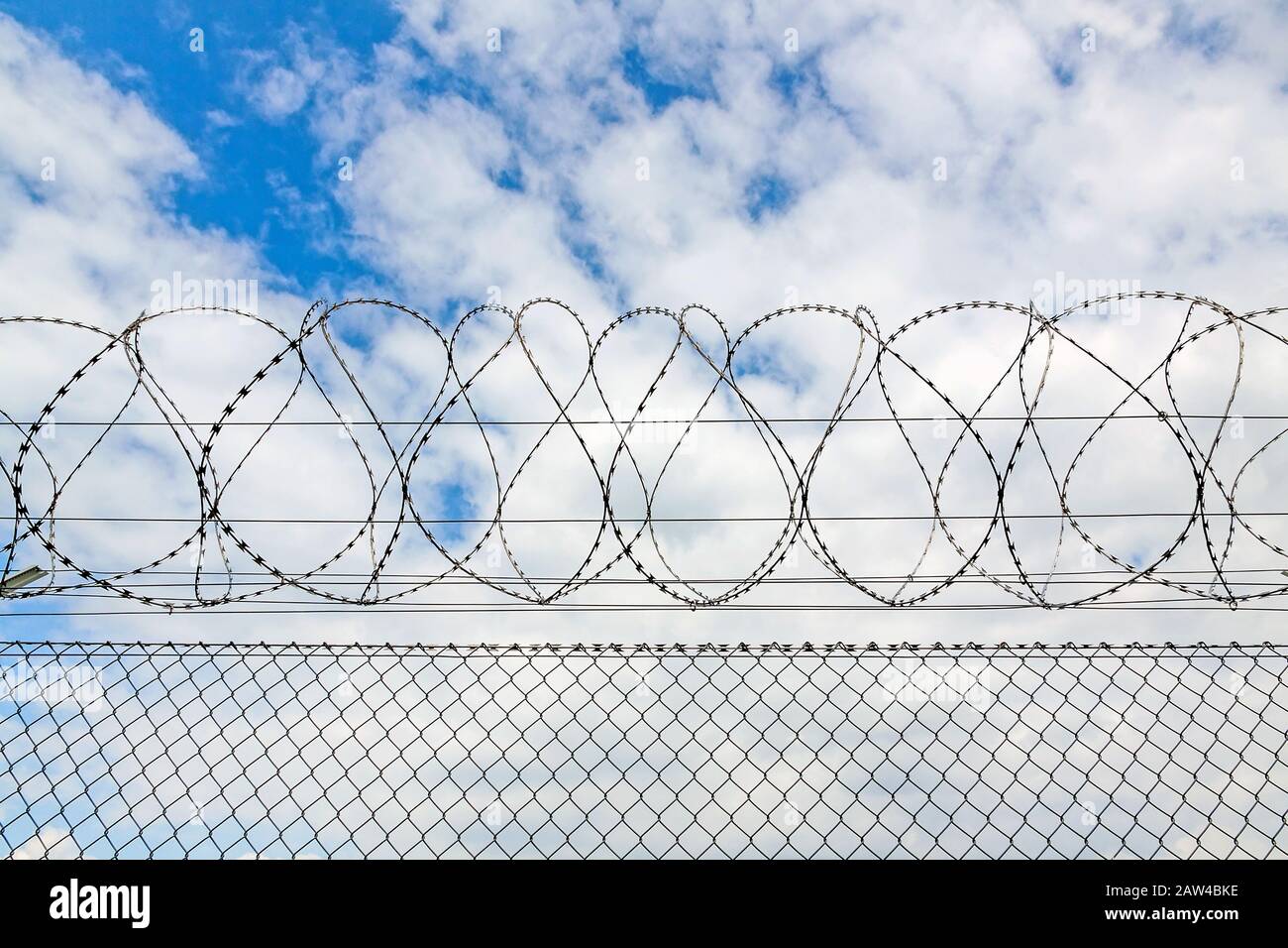 fence with barbed wire against blue sky with clouds Stock Photo - Alamy
