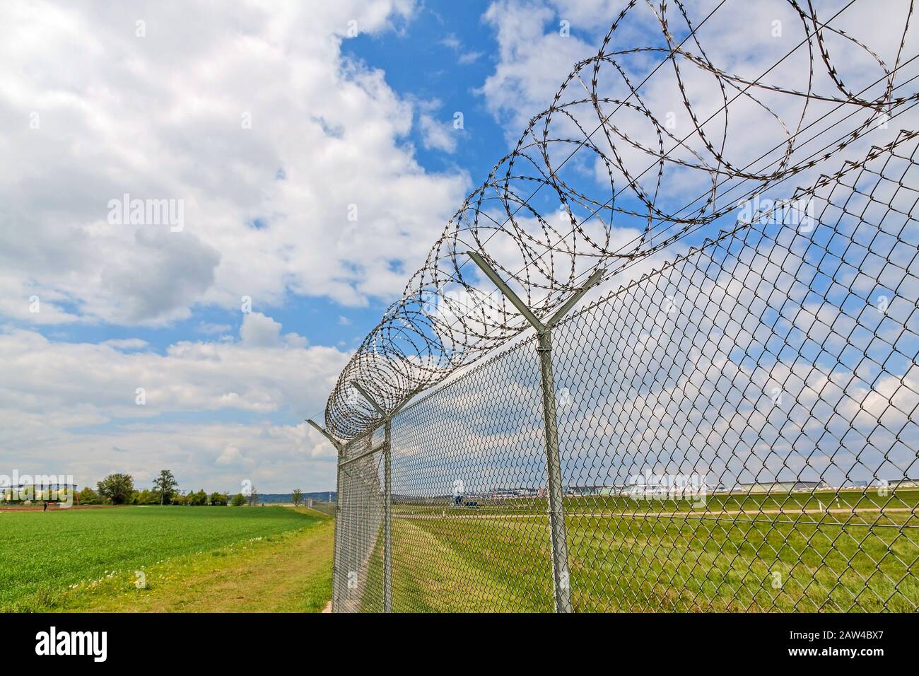 fence with barbed wire, green landscape and blue sky with clouds Stock Photo