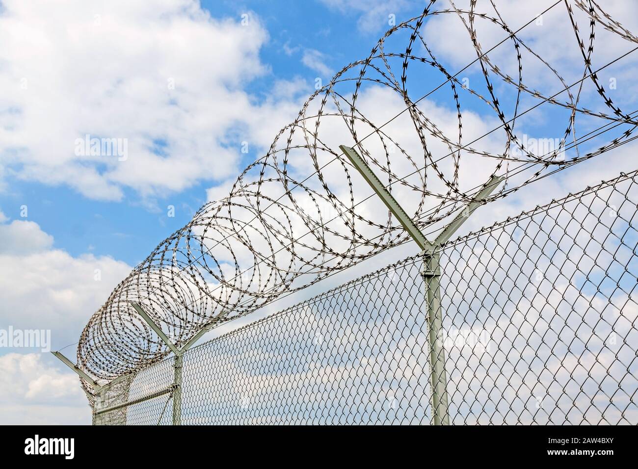 fence with barbed wire against blue sky with clouds Stock Photo