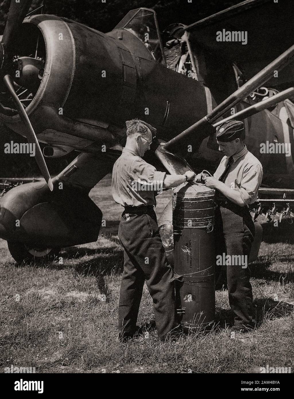 Ground crews preparing a canister of supplies for fitting to a Westland Lysander (nicknamed the 'Lizzie') is a British army co-operation and liaison aircraft produced by Westland Aircraft used immediately before and during the Second World War. The aircraft's exceptional short-field performance enabled clandestine missions using small, improvised airstrips behind enemy lines to place or recover agents, particularly in occupied France with the help of the French Resistance. Stock Photo