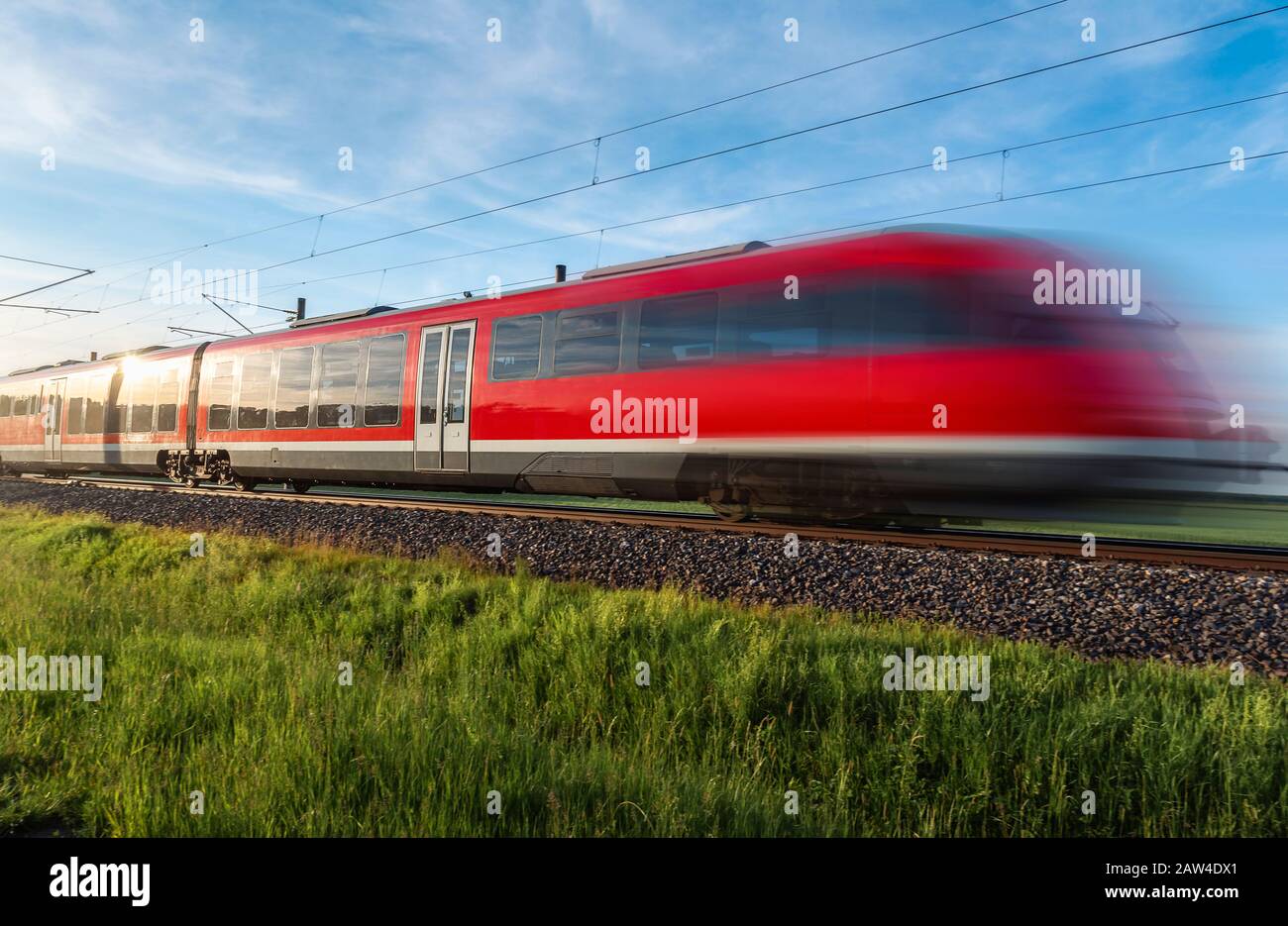 Modern red train, in motion blur, traveling through green nature, german countryside, on summer sunny day, Schwabisch Hall, Germany. Train transport. Stock Photo