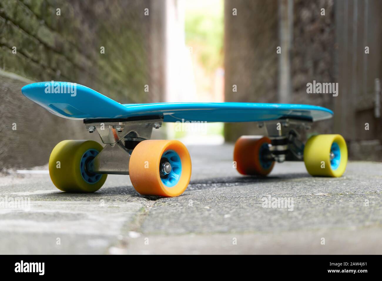 Blue plastic mini cruiser penny board or skate board with yellow and orange  wheels in an alley with light at the end Stock Photo - Alamy