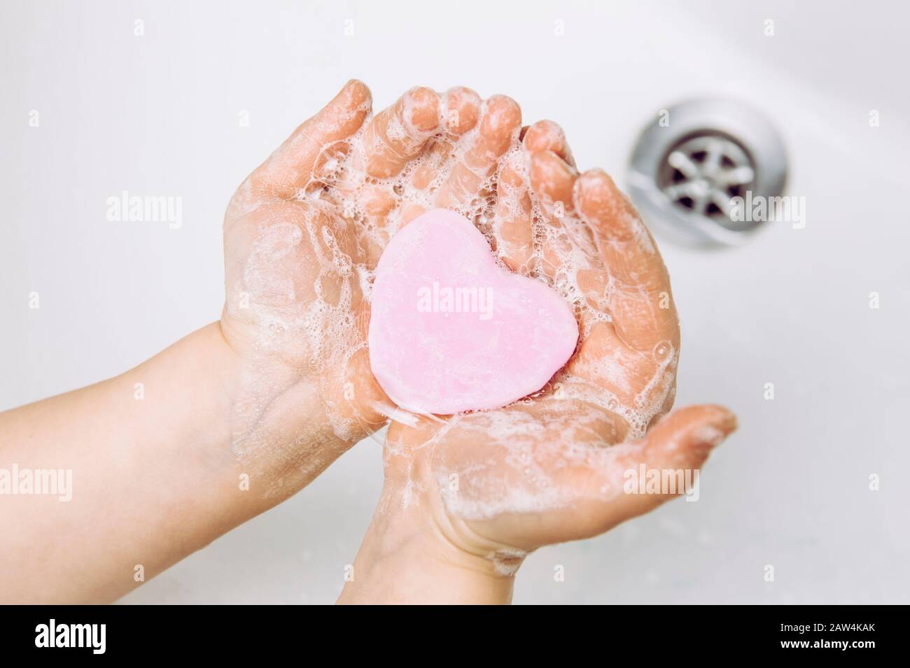 Importance of personal hygiene care. Flat lay view of child washing dirty hands with pink heart shape soap bar, lot of foam. Copy space. Stock Photo