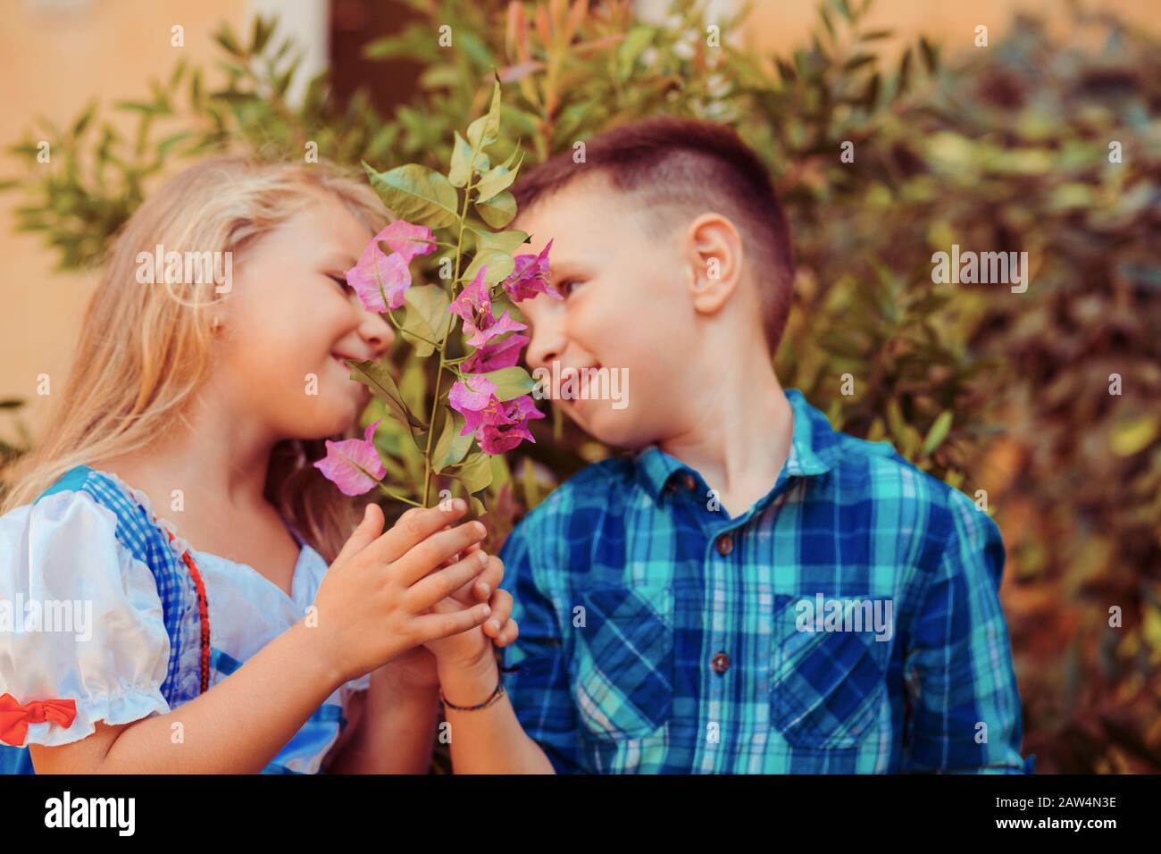 Two children smell the flowers green tree background. Boy brother gives a flower to the girl sister. Love care concept Stock Photo