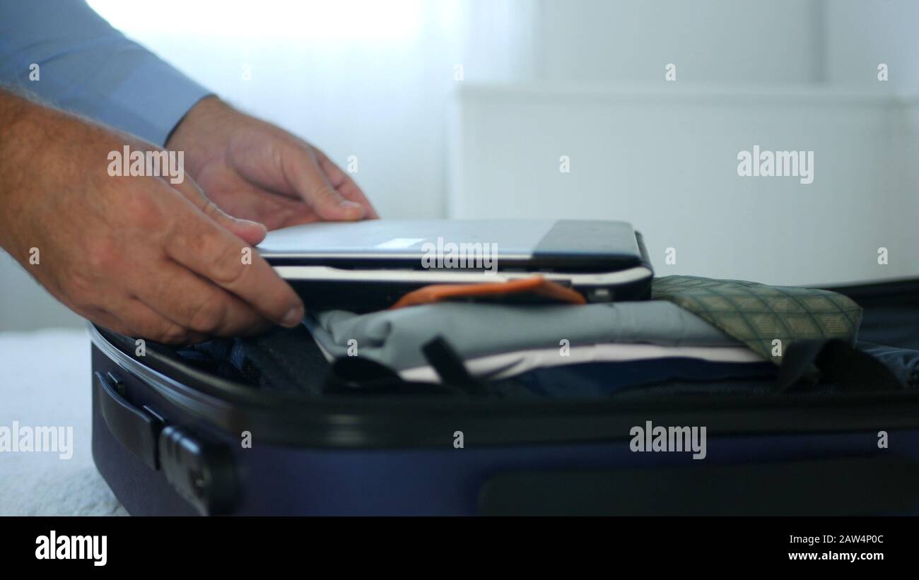 Businessman Put a Laptop in the Suitcase Preparing his Luggage for a Business Trip Stock Photo