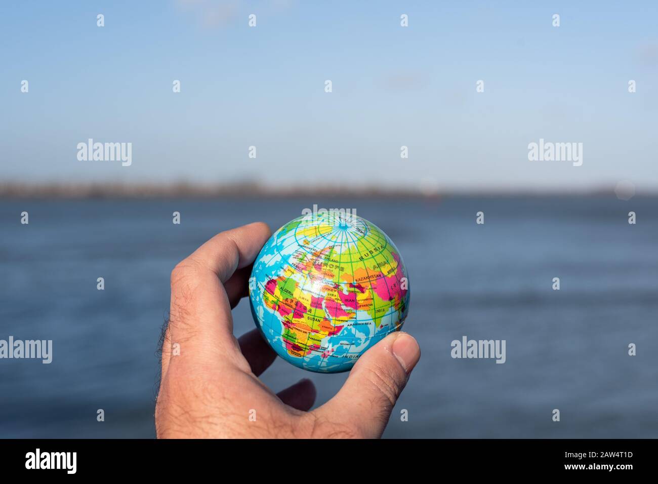 Hand holding a small globe and a lake in the background Stock Photo