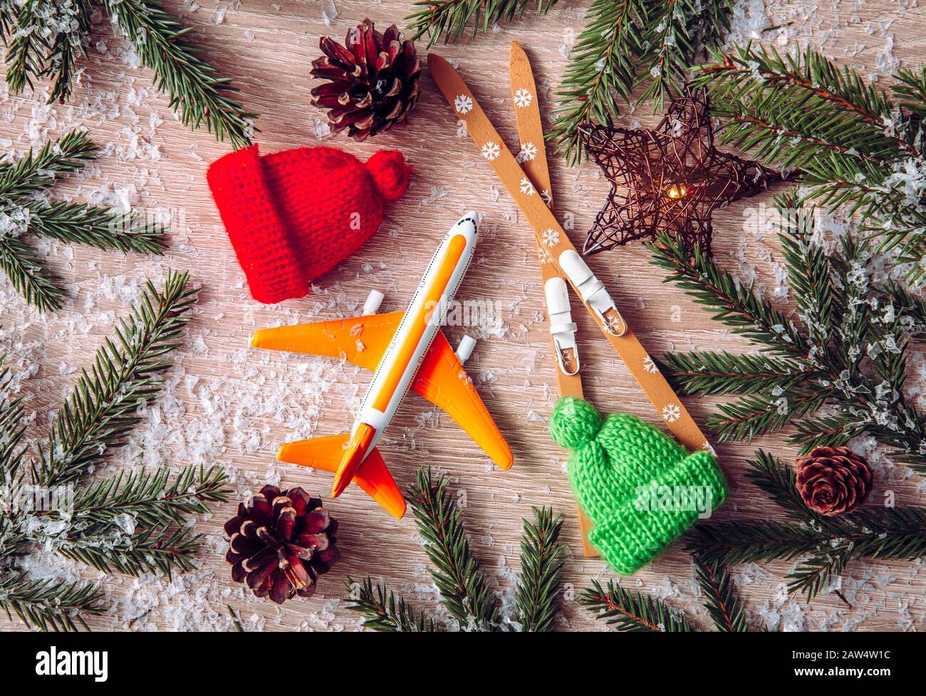 Go on winter ski trip concept. Top view of airplane, skis, beanie hats, spruce tree branches on natural comfortable wood background. Modern orange Ins Stock Photo