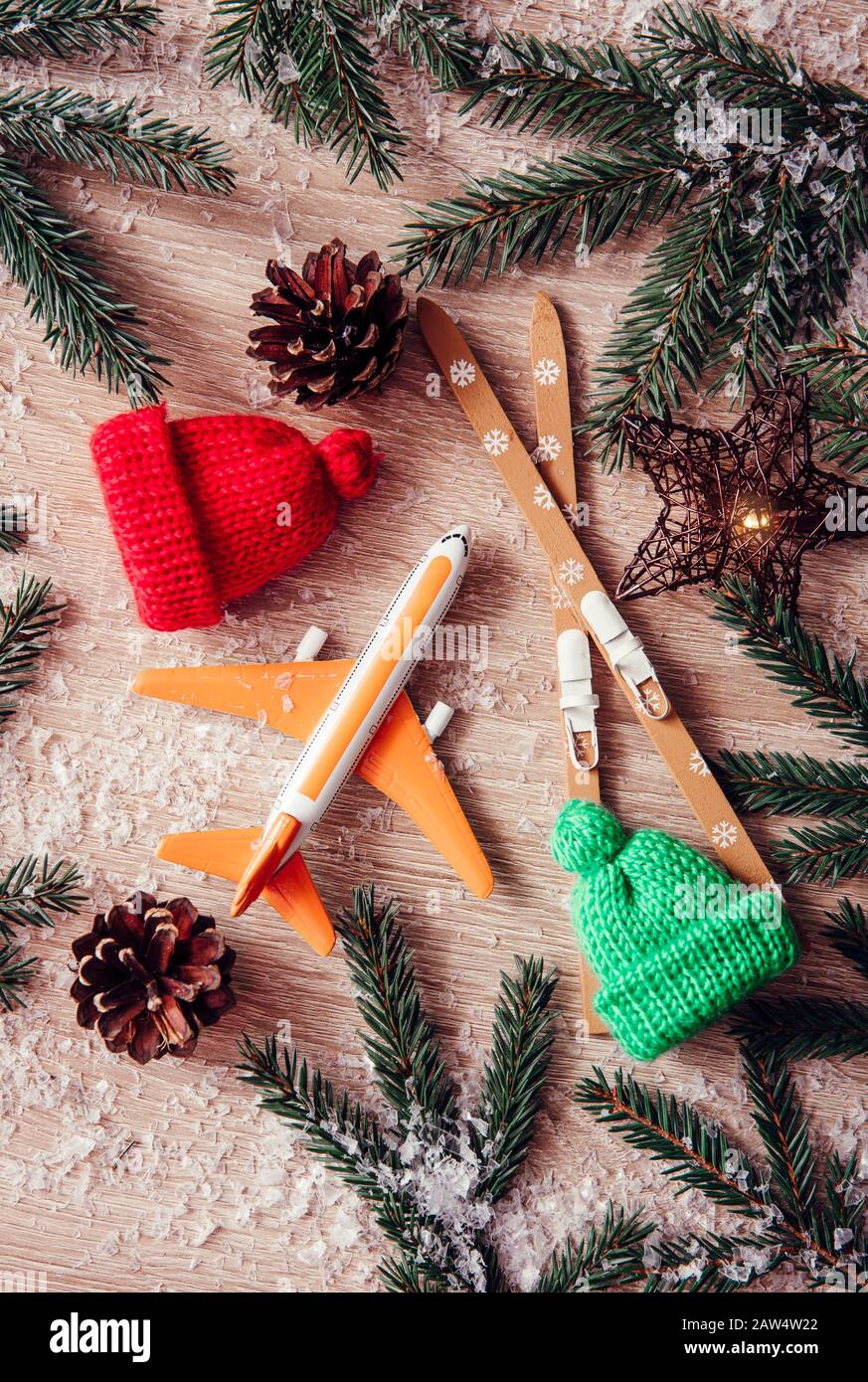 Go on winter ski trip concept. Top view of airplane, skis, beanie hats, spruce tree branches on natural comfortable wood background. Modern orange Ins Stock Photo