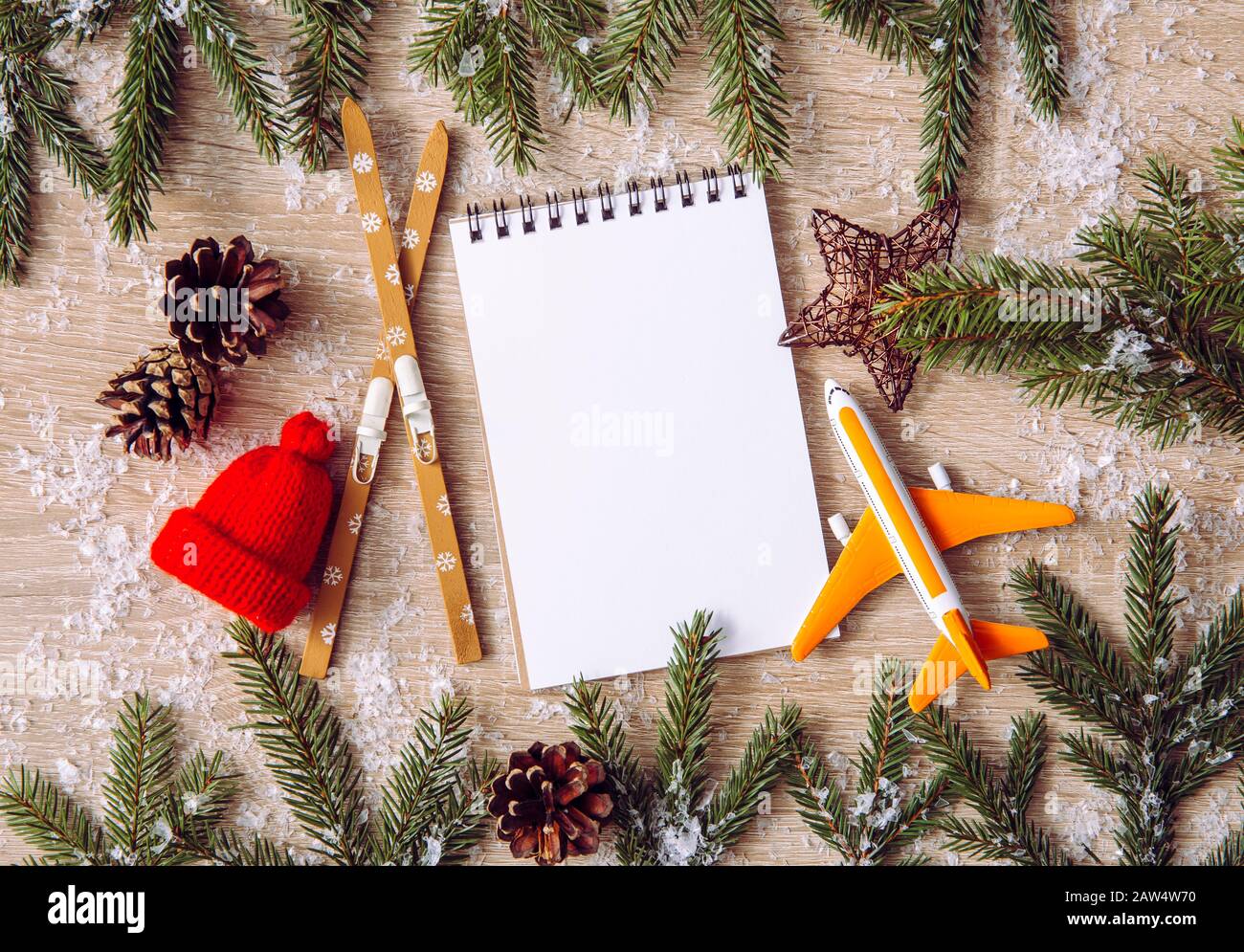 Go on winter ski trip destination. Top view of airplane, skis, beanie hats, spruce tree branches and empty notebook on natural comfortable wood backgr Stock Photo