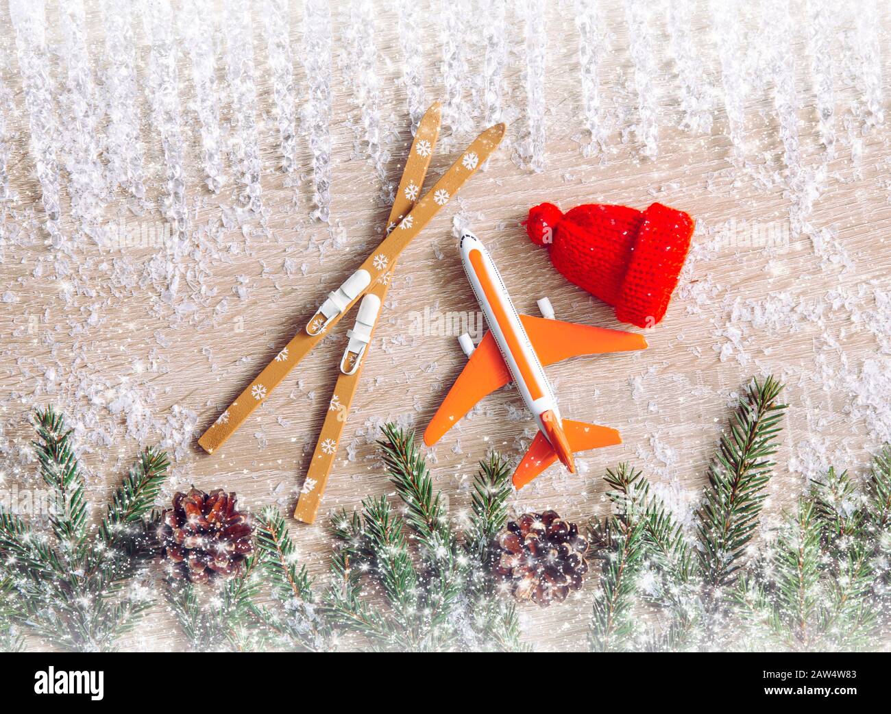Go on winter ski trip concept. Top view of airplane, skis, beanie hats, spruce tree branches on natural comfortable wood background. Stock Photo