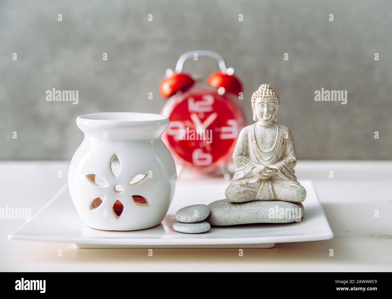 How to find balance between busy life and healthy mental health. Taking a break to sit and meditate concept. Buddha figure with aroma lamp and clock o Stock Photo