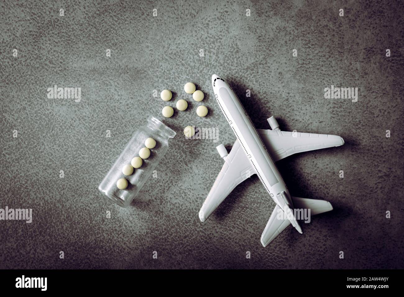 Plane figurine with pills spilled. Travel and medicine concept. Flat lay view with copy space on minimalist gray background. Stock Photo