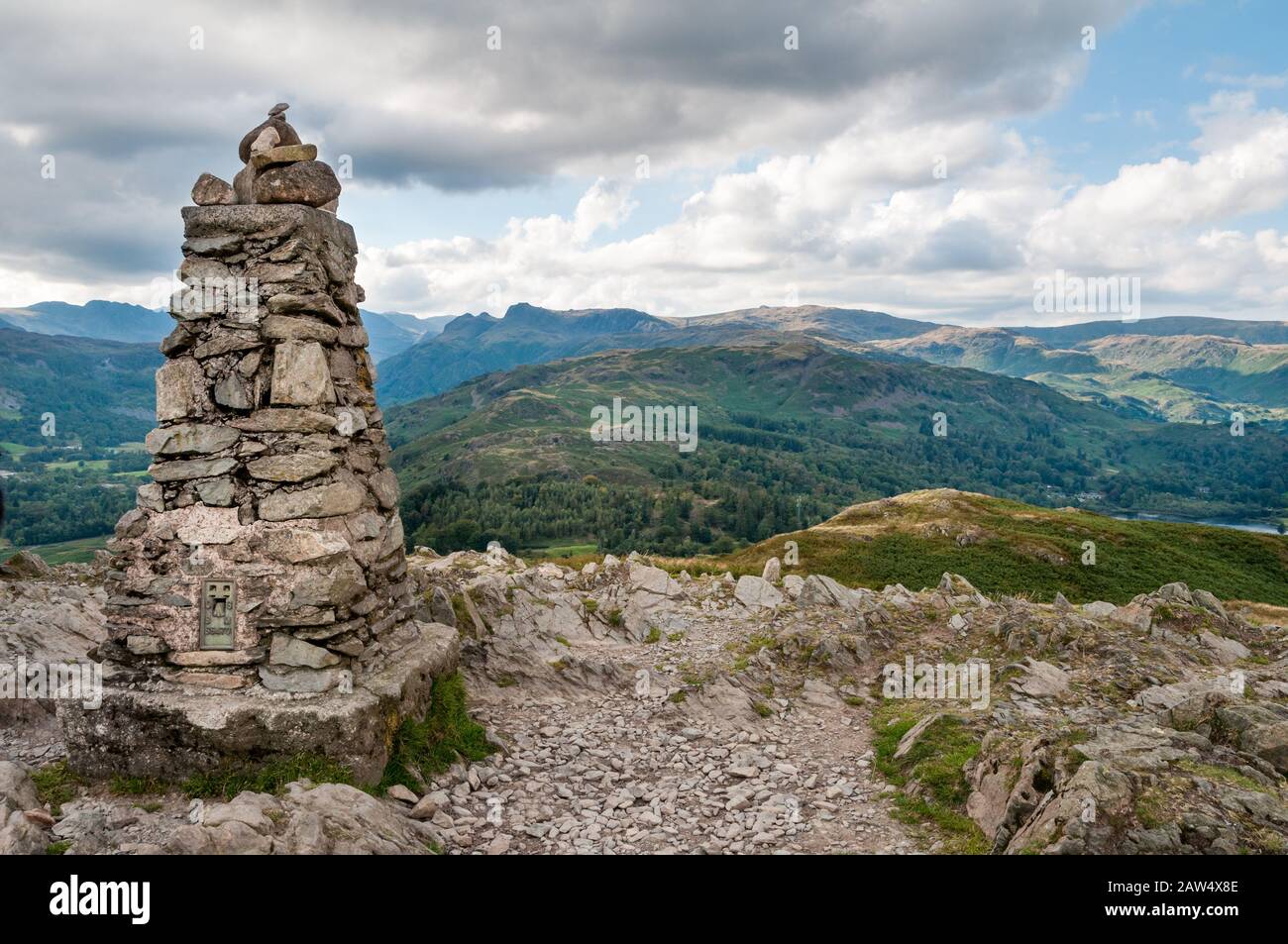 Summit cairn on the top of Loughrigg in the English Lake District with a view of the Langdale Pikes in the distance. Stock Photo